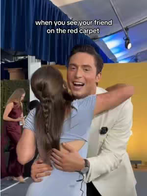 A man hugs a woman on a red carpet, with text overlayed.