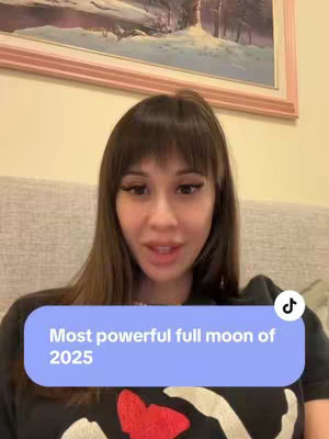 A woman with long brown hair and wearing a dark shirt is centered in the frame, addressing the camera. A blue rectangle with white text overlayed on top of the video is showing the text hook of the video. The background is slightly out of focus and includes a painting and a light colored wall.
