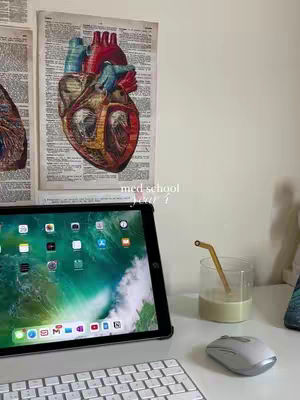 The image shows a workspace with a tablet, keyboard, mouse, and a glass with a straw. Behind them are anatomical drawings of a heart and text overlays.