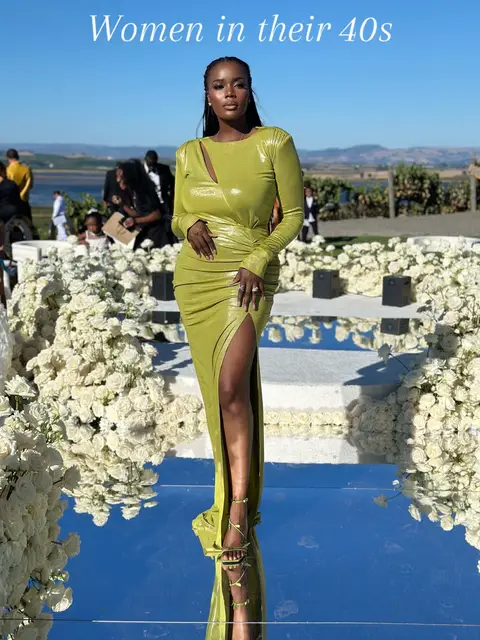 The image features a woman in a lime green, form-fitting gown with a high slit, standing on what appears to be a mirrored surface. She has dark skin, dark hair, and is facing the camera. The background includes a wedding setting, with white floral arrangements and people. The lighting appears natural and bright.