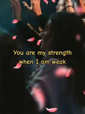 The cover image is a blurred photograph. Soft lighting sets a mood of reverence and contemplation. The main elements consist of an out-of-focus foreground featuring hands raised with the focus on a figure with darker skin, hands raised in worship. Scattered across the scene are pink petal-like shapes, evoking a sense of transition and movement. The text overlayed in the foreground uses a simple font and yellow color text which draws instant attention.
