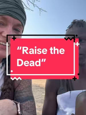 A selfie-style image featuring two people, one on the left with a green head wrap and another on the right with short, dark hair. A red rectangle with white text says "Raise the Dead," overlaid on top of the subjects. Both are smiling, and the background suggests an outdoor setting possibly in a sunny environment.
