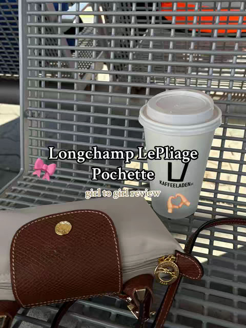 The cover image shows a handbag, a cup of coffee, and a pink bow, set on a metallic grid background. The handbag, a brown pouch style with a gold button, rests next to a small off-white folded bag, resting on a metallic surface. A full cup of coffee is on the right, with the words 'KAFFEELADEN' on it. The text overlays includes the words 'Longchamp LePliage Pochette' and 'girl to girl review'.