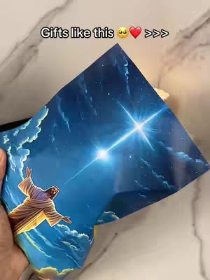 A hand holds an image of Jesus with arms open, set against a blue sky filled with stars. Text overlay at the top reads "Gifts like this 😍❤️ >>>".