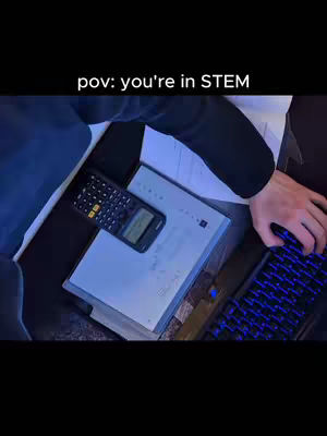A person's hands are shown working on a laptop with a keyboard and some papers/books next to a calculator.