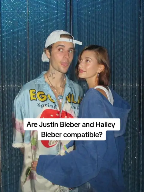 The image features a couple, Justin Bieber and Hailey Bieber, standing in front of a blurred, light-blue patterned background. Justin, on the left, is wearing a white cap, a light blue shirt with graphic designs, and has visible neck tattoos. He sticks his tongue out and appears to be looking to the left. Hailey, on the right, is looking at Justin, with her face turned towards him, wearing a blue hoodie and white top. Text overlay on the cover image reads, "Are Justin Bieber and Hailey Bieber compatible?"