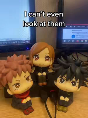 The cover image features three anime figurines, presumably characters from Jujutsu Kaisen, arranged on a wooden surface. The figurines are in a setting with two computer monitors in the background. Overlay text is displayed at the top.