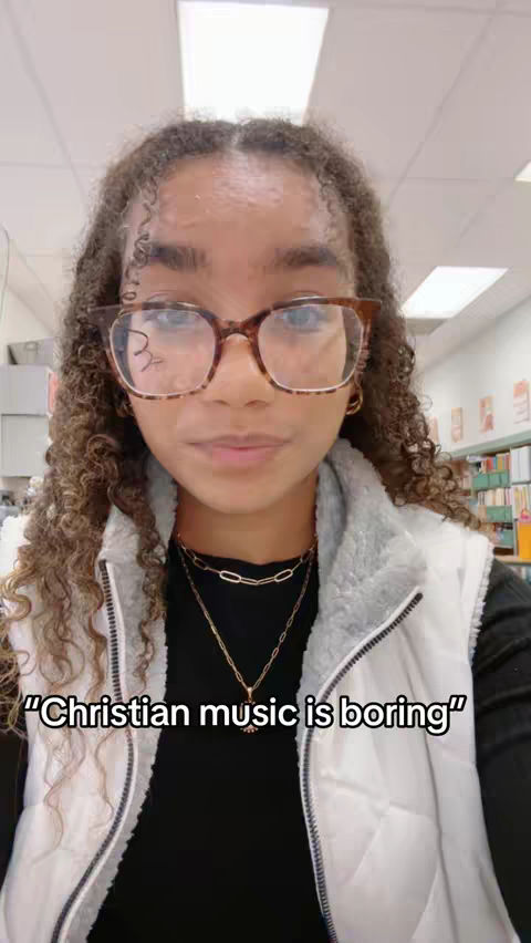 A young woman with curly hair and glasses is the main subject, set against a blurred indoor background. She is wearing a black top, a white vest, and necklaces. Text overlayed at the bottom says "Christian music is boring".