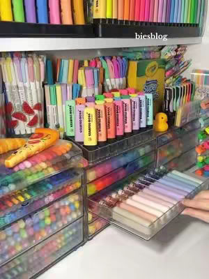 The cover image showcases a meticulously organized display of colorful stationery items. The composition is dominated by various pens, markers, and highlighters arranged on shelves and inside clear drawer organizers. The color palette is vibrant and diverse, with a spectrum of hues ranging from pastels to bold primary colors. The layout emphasizes order and visual appeal, highlighting the aesthetic qualities of the stationery and the satisfaction of organized supplies.