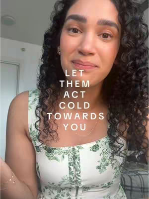 A woman with curly dark hair and a gentle expression is the central focus. She wears a sleeveless, floral print top in white and green. Text overlayed on the image reads, 'LET THEM ACT COLD TOWARDS YOU'.