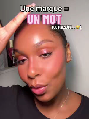 A close-up selfie featuring a woman with dark skin, styled black hair, and full, glossy lips, wearing pink eye makeup and blush. A text overlay arches above her, and her hand is raised near her forehead.