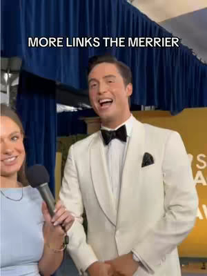 A man in a white suit and black bow tie is being interviewed, with a smiling woman holding a microphone to his side. The background is a blue curtain with gold accents. The man is laughing, and the overlay text reads: MORE LINKS THE MERRIER.