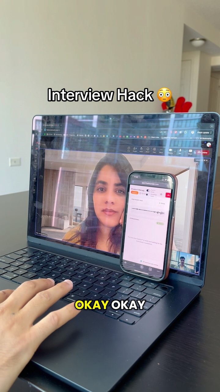 The cover image shows a laptop displaying a video call with a woman on the screen, while a hand types on the keyboard. A smartphone rests beside the laptop, displaying an app interface. The words "Interview Hack 🤔" are written at the top in bold while "OKAY OKAY" is at the bottom.