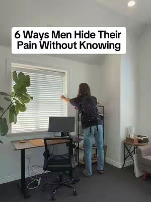 A room with a window and blinds is shown. A person is leaning against the window, near a desk with a computer. The text overlay reads "6 Ways Men Hide Their Pain Without Knowing".