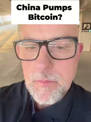 A selfie-style shot featuring a man in front of a parking garage setting, where the foreground shows the man with glasses and a beard, and in the background, a sign is visible.