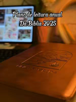 The cover image shows a close-up of a closed, brown Bible on a wooden surface. Above it is a computer screen displaying a blurred image. Text overlays the image, indicating a reading plan for the year 2025. The lighting suggests a warm, focused environment.