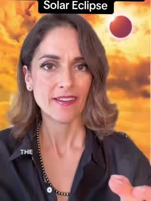 A woman with brown hair and dark eyes smiles at the camera. She wears a black top and a beaded necklace. Behind her is a blurry background with a warm, orange and yellow color scheme, a solar eclipse graphic is overlaid. The words "Solar Eclipse" are above her.