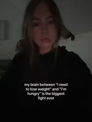 A blurry, low-light selfie taken from a slightly low angle shows a woman in a black hoodie. Text is overlaid at the bottom, and the overall composition is dim and focused on the subject's face.