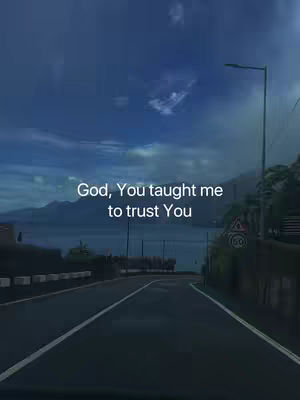 A road stretches towards the horizon, framed by a roadside and a backdrop of a lake and mountains under a cloudy blue sky. The words 'God, You taught me to trust You' are overlaid on the image.