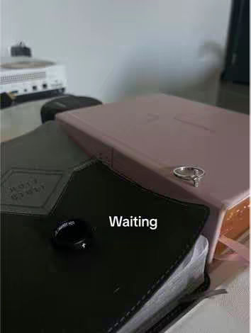 The image shows a close-up of a Bible with a ring resting on top and the word "Waiting" in the image. The background is blurred with neutral colors.
