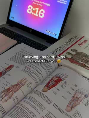 The image shows a laptop open with a clock on screen. In front of the laptop are the open pages of a human anatomy textbook with detailed illustrations of muscles and bones. A caption is overlaid on the textbook pages.
