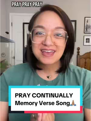 A woman with glasses smiles and speaks to the camera, with text overlayed at the bottom that reads "PRAY CONTINUALLY Memory Verse Song". The background is a room with a white door and framed pictures.