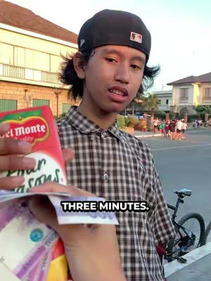 A young man wearing a black cap and a checkered shirt holds money and a Del Monte Four Seasons juice pack. The image is taken outdoors, with a blurred background of buildings and pedestrians.
