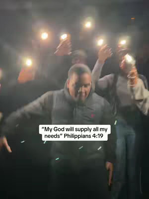 The cover image features a group of people, primarily focused on a man in the center who is smiling and looking down. The background is dark, but several individuals are holding up bright lights or phones, creating a glowing effect around them. Overlayed in the image is text that appears to be a quote from the Bible.