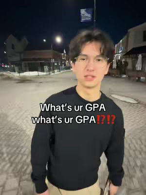 A young man wearing glasses and a black sweater stands on a city street at night. Text overlays on the image, posing a question and asking about GPA. The background shows buildings and streetlights.
