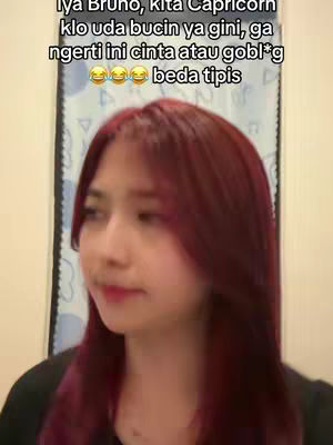 A young woman with long, dark red hair and a black top is shown from the chest up, looking slightly off-camera. Text overlays with Indonesian text are positioned at the top. The background is a patterned wall.