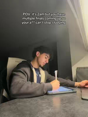 A young man is sitting at a desk, illuminated by soft light from overhead. The scene focuses on him as he appears to be studying with a digital tablet. The text overlay provides context, framed against a dark background with the room's features dimly visible.