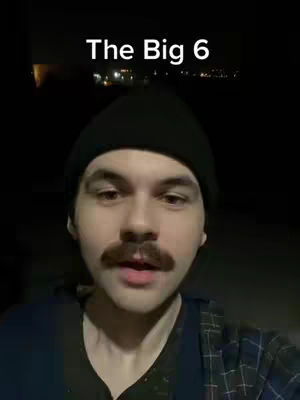 The cover image features a medium shot of a man wearing a black beanie. The background is dark, with some indistinct lights, possibly suggesting an outdoor or nighttime setting. The man has a prominent mustache and is looking directly at the camera. The overlay text reads "The Big 6".