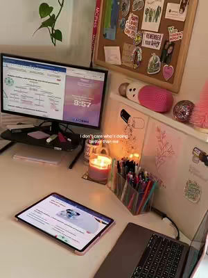 The image showcases a well-lit desk setup. A computer displaying a webpage with a purple-themed background. Next to it, an open laptop and a tablet lie flat, also displaying content. A candle is lit, lending a warm ambiance, surrounded by pens and decorative items. The scene suggests a study environment.