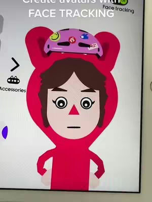 The image is a screen capture from a mobile device or tablet, showing the creation of an avatar. The central figure is a cartoon avatar in a red hooded outfit, with a matching red face mask. Its face is simply illustrated with big circular eyes with eyelashes, a small red triangle for its nose, and a straight line for the mouth. The top of the avatar's head has a decorative helmet. Additional display elements include a menu of accessories and textual options around the avatar builder's interface. The background shows a white color.