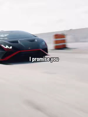 A black sports car is driving on a cement road. The car's front end with red trim is prominent on the left side of the screen. In the background, there are orange and white traffic barrels to the right, with a slightly blurred look, and a white background. The text 'I promise you' appears in a white box near the bottom of the image.
