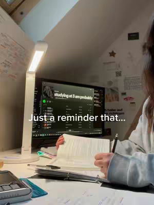 A person studies with a book. A computer monitor displays an app’s interface. Text overlays read, "Just a reminder that..."”, "studying at 3 am probably". A table lamp faces the scene with soft lighting.