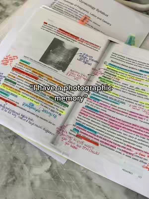 The image shows an open textbook with highlighted notes and annotations. A handwritten quote is overlaid on the book reading 'I have a photographic memory.' The book is on a light surface, possibly a desk or table, with additional sheets of paper visible in the background.