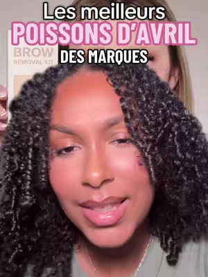 The cover image shows a close-up of a woman's face with dark, curly hair and a slight smile. Text overlays at the top in all caps, reads: 'Les meilleurs poissons d’avril' in pink, and 'des marques' in white, and the year '2025' is in white. Behind the woman’s face, there is another woman’s face blurred out. The overall composition emphasizes the subject's features with a focus on her lips and eyes.