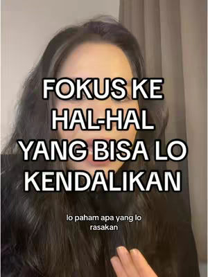 A selfie-style shot of a woman with long dark hair. The main focus is her face, overlaid with large, white text promoting self-improvement. Below the text, there is a smaller text that appears to complete the thought. The background is simple, with a neutral tone that provides no distinct features. The overall composition relies on the text overlay to deliver the message.