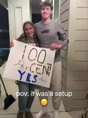 Two young people standing close together while holding up a sign that reads "100 Percent YES" in large letters made of pennies. One person is holding the sign while the other is smiling.