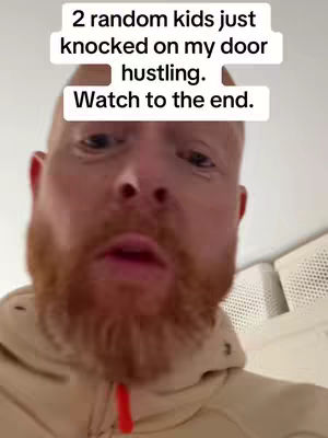 A man with a red beard, wearing a tan hoodie, is centered in a selfie shot. The background is a light-colored wall with an air vent visible to the right. White text appears in two rectangular boxes above and below the man's head, with the top box stating '2 random kids just knocked on my door hustling.' The bottom box urges the viewer to 'Watch to the end.'