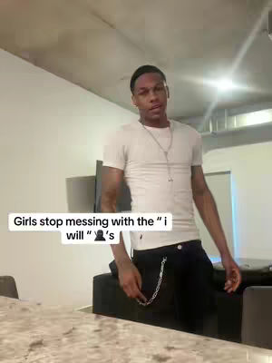 A young Black man stands casually in a room, wearing a white t-shirt and black pants. Text overlays appear at the bottom of the image. The lighting is bright and the composition is simple, focusing on the figure.