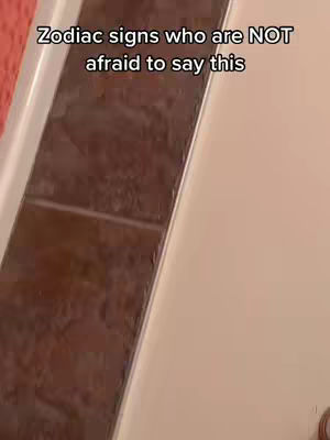 The image shows a close-up shot of a white wall and a tiled surface at an angle. The tiled area is brown and rectangular. The text overlay on the image reads the text: "Zodiac signs who are NOT afraid to say this".