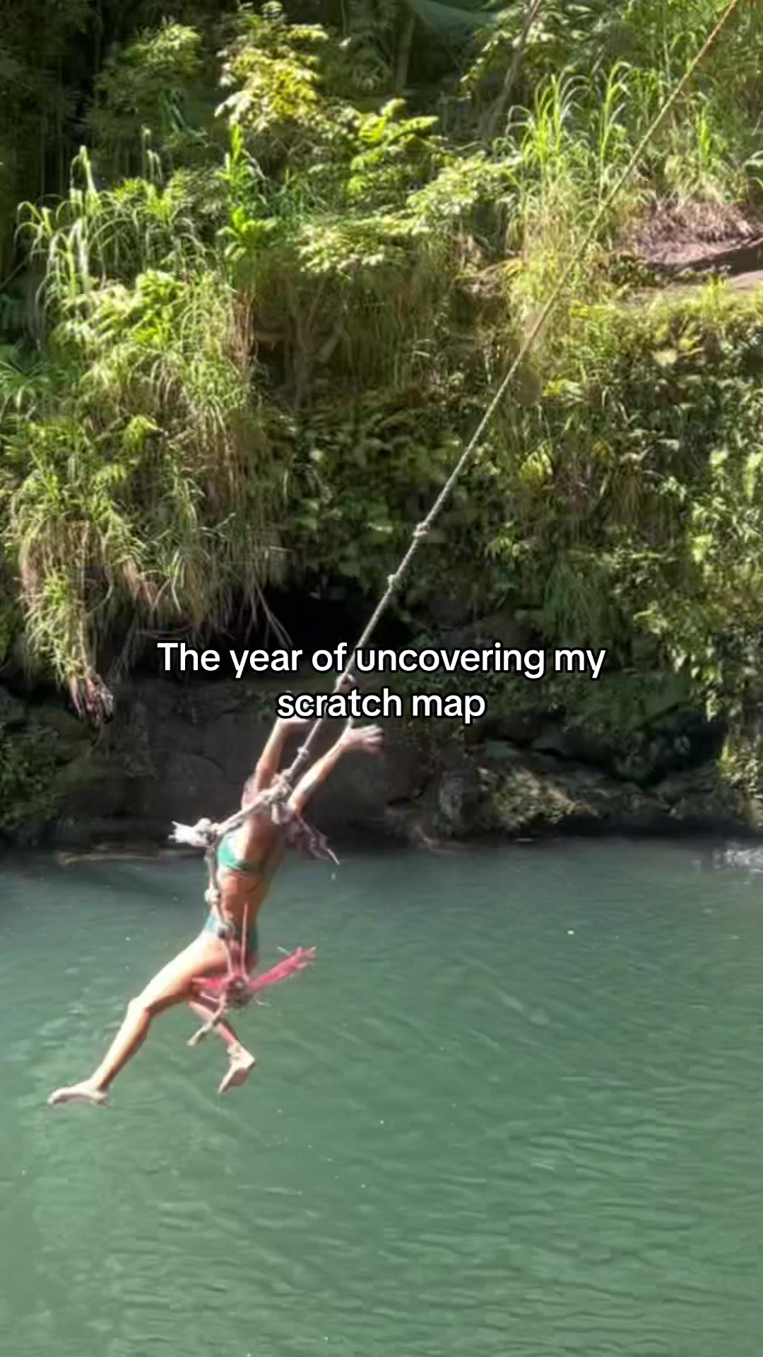 A person hanging from a rope swing over water, with lush green foliage in the background and text overlayed at the top.