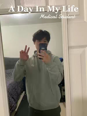 The cover image shows a young man taking a selfie in a mirror. He's wearing a gray hoodie and making a peace sign with his right hand while holding a phone up with his left hand, partially obscuring his face. The mirror reflects a glimpse of a bedroom setup, and text overlays at the top read 'A Day In My Life' and 'Medical Student'.
