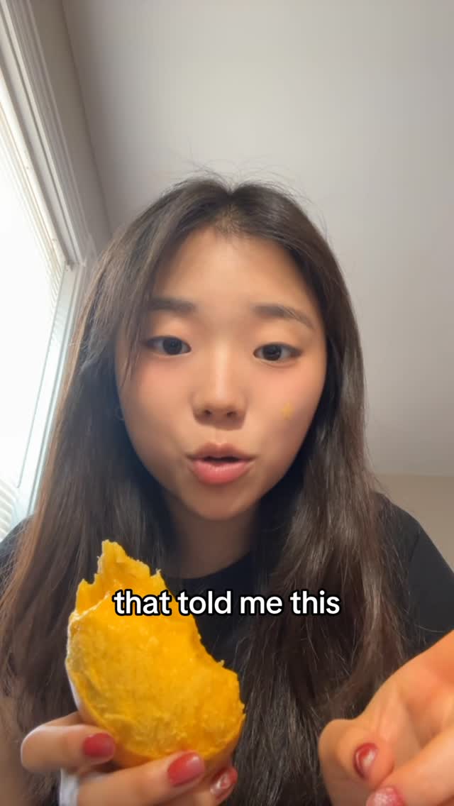 A young woman with long dark hair and fair skin is holding a large piece of a yellow fruit, possibly a mango, near her face. The text "that told me this" is superimposed over the fruit. The background is blurred, suggesting an indoor setting.