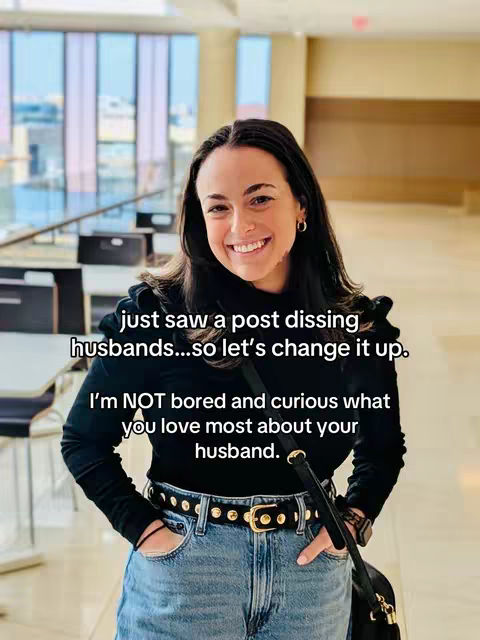 A woman with dark hair and a slight smile stands indoors, hands in pockets, facing the camera. She is wearing a black top, a belt with a gold buckle, and blue jeans. Text overlays the image in a sans-serif font.