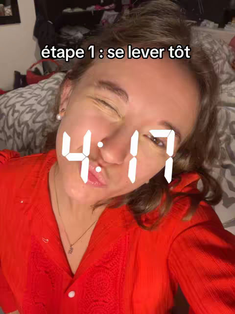 A selfie-style shot features a woman's face close-up against a blurred background. The woman is winking, with the time 4:17 displayed prominently over her face in a digital font. The background hints at an indoor setting with a bed visible.