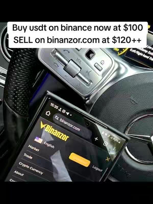 A screenshot of a phone displaying a trading platform website is held over a car's steering wheel. The phone screen prominently features the website binanzor.com. Above the phone, the car's control panel and steering wheel are visible, with the text overlay instructing the viewer on crypto trading strategies.