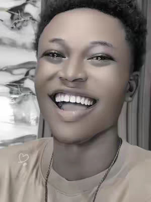 A selfie featuring a young person smiling widely, with visible teeth and a closed-mouth smile. The background is out of focus and appears to have floral elements. The lighting is soft and even.
